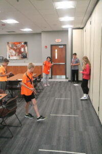 A group performing measurements on a remote car using tape on the floor